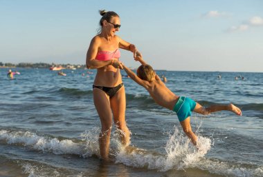 Genç anne ve sahilde oyun gün süresi içinde gülümseyen bebek çocuk evlat. Olumlu insan duyguları, duygular, joy. Tatil yapma ve yaz zevk komik şirin çocuk. Bahar ve yaz tatil.