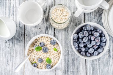 Beyaz ahşap beton arka plan kopya alanı sağlıklı tahıl ve süt kahvaltı kavramı, süt ve taze yaban mersini, küçük kase kuru yulaf