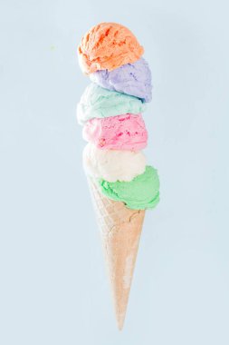Pastel renkli dondurma külahları açık mavi arka planda izole edilmiş. Kadın eli farklı aromalı büyük dondurma külahını tutuyor.