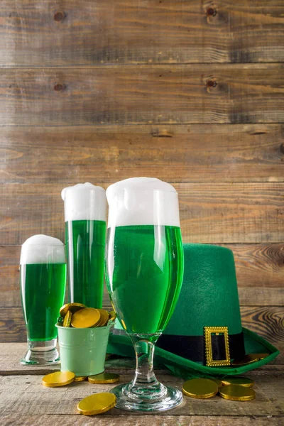 Traditional irish alcohol for St Patrick\'s day party. Different glasses with green beer, with golden chocolate coins decor and green leprechaun hat. Old rustic wooden background copy space