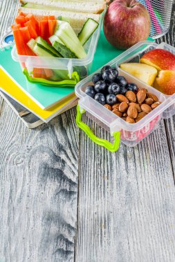 Sağlıklı bir okul yemeği kutusu. Sandviç, meyve, sebze, fındık, su ve okul malzemeleri ile çocuk öğle yemeği kutusu, Beyaz ahşap arka plan