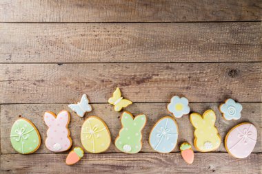 Pastel renkli Paskalya kurabiyeleriyle mutlu paskalya arkaplanları - tavşanlar, yumurtalar, çiçekler, kelebekler, ahşap kırsal arka plan, düz afiş alanı