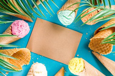 Dondurmalı waffle külahında çeşitli parlak renkli dondurma seti. Çikolatalı, yabanmersinli, şam fıstıklı, trend turkuaz arka planda ve tropikal palmiye yapraklı.