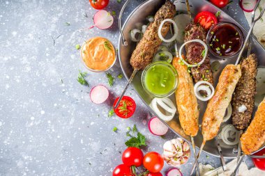 Yaz bbq partisi. Çubukta şiş kebap, kıyma ve tavuk etinden. Lula kebap, geleneksel Kafkas Asya yemeği. Çeşitli soslar, baharatlar ve domateslerle, gri taş arka plan, yukarıdaki boşluğu kopyala 