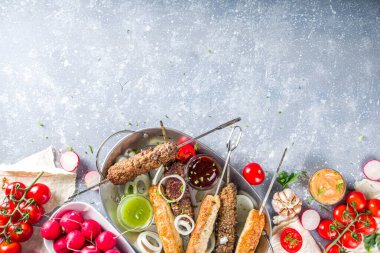 Yaz bbq partisi. Çubukta şiş kebap, kıyma ve tavuk etinden. Lula kebap, geleneksel Kafkas Asya yemeği. Çeşitli soslar, baharatlar ve domateslerle, gri taş arka plan, yukarıdaki boşluğu kopyala 