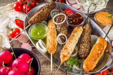 Yaz bbq partisi. Çubukta şiş kebap, kıyma ve tavuk etinden. Lula kebap, geleneksel Kafkas Asya yemeği. Çeşitli soslar, baharatlar ve domateslerle, gri taş arka plan, yukarıdaki boşluğu kopyala