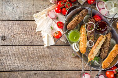 Yaz bbq partisi. Çubukta şiş kebap, kıyma ve tavuk etinden. Lula kebap, geleneksel Kafkas Asya yemeği. Çeşitli soslar, baharatlar ve domateslerle, gri taş arka plan, yukarıdaki boşluğu kopyala