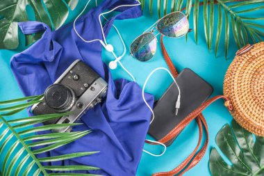 Summer vacation and travel concept. Beach accessories things - bag, hat, swimsuit, sunglasses, camera, tropical leaves on aquamarine, turquoise blue backdrop. Summer is coming trendy concept