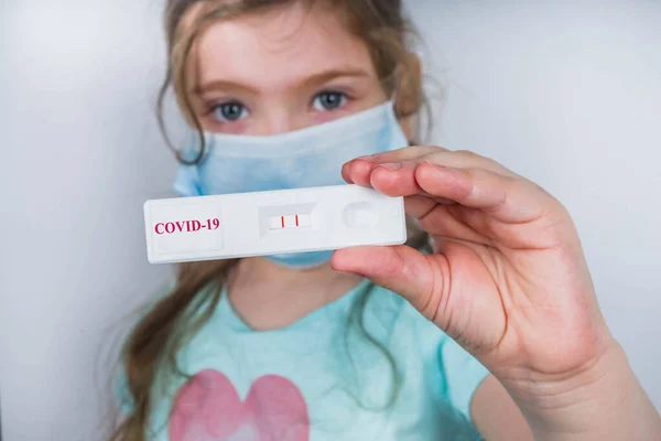 Worldwide coronavirus epidemic concept. Pandemic COVID-19, 2019-nCoV. Kid girl with positive test strip for antibody or sars-cov-2 virus disease in hands. White background