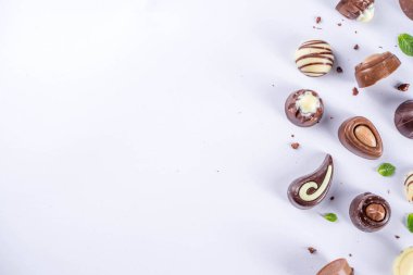 Beyaz arka planda çeşitli çikolata şekerleri. Farklı tatlı ve nane yapraklı çikolatalar, kopyalama alanı, basit desen düzeni 