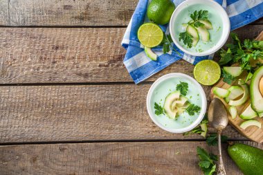 Ev yapımı avokado kremalı çorba, limon, otlar ve ahşap arka planda avokado dilimleri, kopyalama alanı