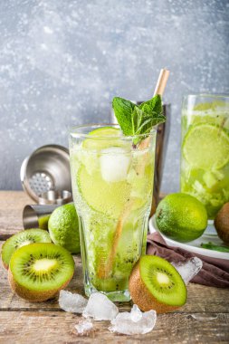 Soğuk yaz içeceği ve içecek tarifleri. Kiwi Lime Mojito kokteyli ya da limonlu alkolsüz moktail, naneli ve dilimlenmiş kivi meyveleri ahşap arka planda fotokopi alanı
