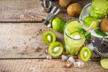 Soğuk yaz içeceği ve içecek tarifleri. Kiwi Lime Mojito kokteyli ya da limonlu alkolsüz moktail, naneli ve dilimlenmiş kivi meyveleri ahşap arka planda fotokopi alanı