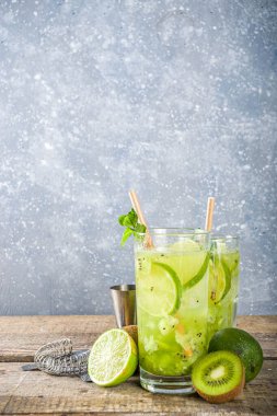 Soğuk yaz içeceği ve içecek tarifleri. Kiwi Lime Mojito kokteyli ya da limonlu alkolsüz moktail, naneli ve dilimlenmiş kivi meyveleri ahşap arka planda fotokopi alanı