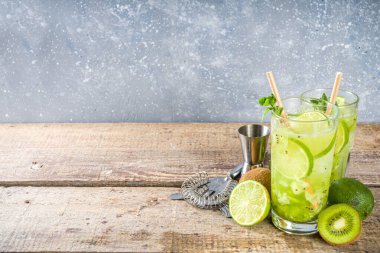 Soğuk yaz içeceği ve içecek tarifleri. Kiwi Lime Mojito kokteyli ya da limonlu alkolsüz moktail, naneli ve dilimlenmiş kivi meyveleri ahşap arka planda fotokopi alanı