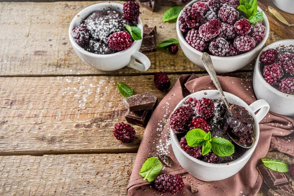Homemade chocolate mug cake with blackberry. Breakfast easy snack recipe, chocolate non dairy cake in mugs, with blackberry, sugar powder and mint, wooden rustic background