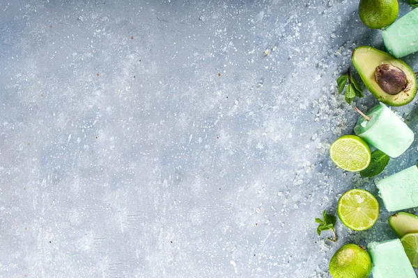 Homemade avocado popsicle. Vegan non-dairy ice cream. Avocado,lime and coconut healthy popsicle on grey stone background with fresh lime slices, avocados and ice