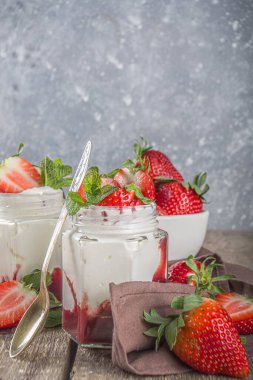 Küçük porsiyonlu kavanozlarda çilekli ve çilekli tatlı sağlıklı yoğurt, ahşap kırsal masada, kopyalama alanı.