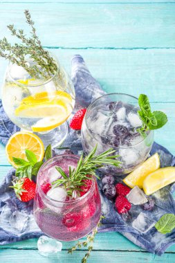 Yaz soğuk içecek konsepti. Meyve ve böğürtlen, cin tonik, limonata moktail, taze yaban mersini, ahududu, limon ve otlar, mavi yeşil ahşap arka plan fotokopi alanı
