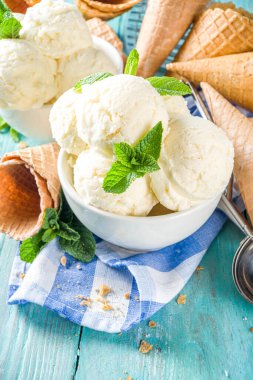 Küçük porsiyonlu beyaz kasede nane yapraklı ev yapımı vanilyalı dondurma topları. Dondurmalı waffle külahı ve kaşıkla, kırsal turkuaz ahşap masa üzerinde, boşluğu kopyala