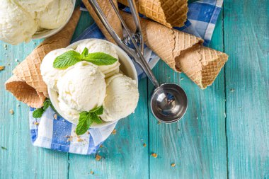Küçük porsiyonlu beyaz kasede nane yapraklı ev yapımı vanilyalı dondurma topları. Dondurmalı waffle külahı ve kaşıkla, kırsal turkuaz ahşap masa üzerinde, boşluğu kopyala