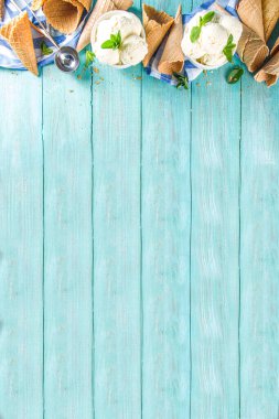 Küçük porsiyonlu beyaz kasede nane yapraklı ev yapımı vanilyalı dondurma topları. Dondurmalı waffle külahı ve kaşıkla, kırsal turkuaz ahşap masa üzerinde, boşluğu kopyala