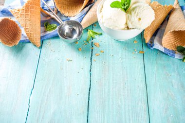 Küçük porsiyonlu beyaz kasede nane yapraklı ev yapımı vanilyalı dondurma topları. Dondurmalı waffle külahı ve kaşıkla, kırsal turkuaz ahşap masa üzerinde, boşluğu kopyala