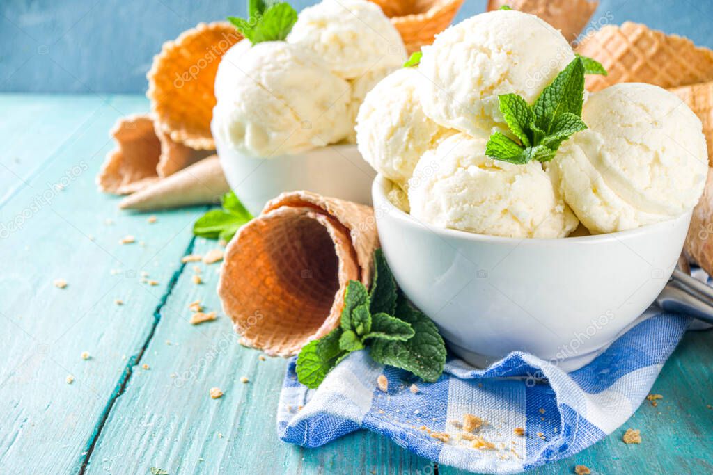 Homemade white vanilla ice cream balls with mint leaves in small portioned white bowl. With ice cream waffle cone and spoon,  on rustic turquoise wooden table, copy space