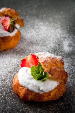 Yaz tatlıları. Ev yapımı pişirme. Krem şantili kek profiterolleri, taze çilekler, nane ve üzerine pudra şekeri serpiştirilmiş. Siyah taş bir masanın üzerinde. Boşluğu kopyala