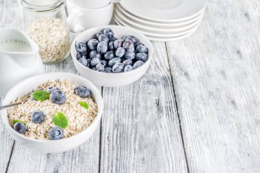 Beyaz ahşap beton arka plan kopya alanı sağlıklı tahıl ve süt kahvaltı kavramı, süt ve taze yaban mersini, küçük kase kuru yulaf