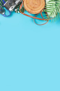 Summer vacation and travel concept. Beach accessories things - bag, hat, swimsuit, sunglasses, camera, tropical leaves on aquamarine, turquoise blue backdrop. Summer is coming trendy concept