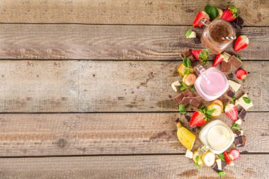 Üç tane milkshake ya da smoothie ile mason kavanozu. Sağlıklı yaz kahvaltısı, öğle yemeği içecekleri - muz, çikolata ve ahşap arka planda çilekli milkshake.