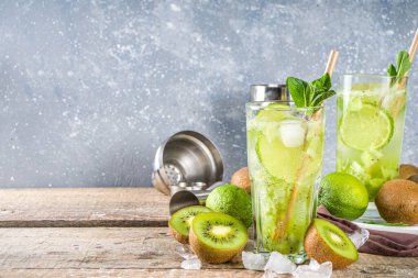 Soğuk yaz içeceği ve içecek tarifleri. Kiwi Lime Mojito kokteyli ya da limonlu alkolsüz moktail, naneli ve dilimlenmiş kivi meyveleri ahşap arka planda fotokopi alanı