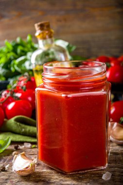 Fesleğen, sarımsak ve taze domatesli ev yapımı domates sosu. Ketçap, küçük kavanozlarda marinara sosu. Tahta bir arka planda, taze sebze ve fesleğenle.