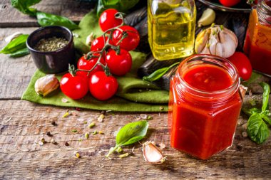 Fesleğen, sarımsak ve taze domatesli ev yapımı domates sosu. Ketçap, küçük kavanozlarda marinara sosu. Tahta bir arka planda, taze sebze ve fesleğenle.