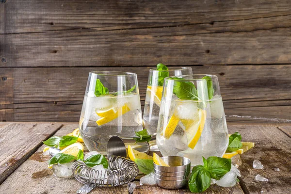 Boozy lemon basil lemonade, with fresh basil leaves, lemons and crushed ice, rustic wooden background copy space