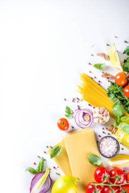 Makarna pişirmek için İtalyan yemekleri. Çeşitli malzemeli çiğ spagetti makarna - soğan, domates, sarımsak, fesleğen, maydanoz, peynir, zeytinyağı. Beyaz tablo arkaplanında, düz kopya alanı