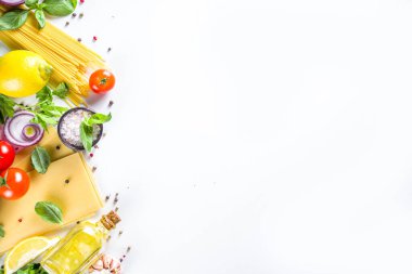 Makarna pişirmek için İtalyan yemekleri. Çeşitli malzemeli çiğ spagetti makarna - soğan, domates, sarımsak, fesleğen, maydanoz, peynir, zeytinyağı. Beyaz tablo arkaplanında, düz kopya alanı