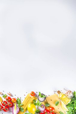 Makarna pişirmek için İtalyan yemekleri. Çeşitli malzemeli çiğ spagetti makarna - soğan, domates, sarımsak, fesleğen, maydanoz, peynir, zeytinyağı. Beyaz tablo arkaplanında, düz kopya alanı