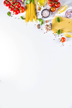 Makarna pişirmek için İtalyan yemekleri. Çeşitli malzemeli çiğ spagetti makarna - soğan, domates, sarımsak, fesleğen, maydanoz, peynir, zeytinyağı. Beyaz tablo arkaplanında, düz kopya alanı