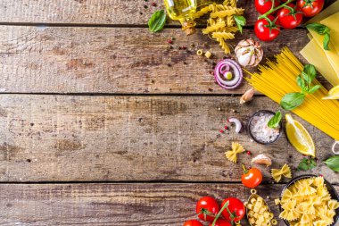 Çeşitli çiğ makarna ve baharatlar. Taze otlar ve sebzelerle İtalyan makarnası pişirmek. Rustik biçim, ahşap arkaplan üst görünüm kopyalama alanı