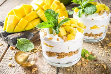 Yaz kahvaltısı, mango ve granola katmanlı tatlı. Porsiyonlu kavanozlarda mango parfe, rustik ahşap arkaplan kopyalama alanı