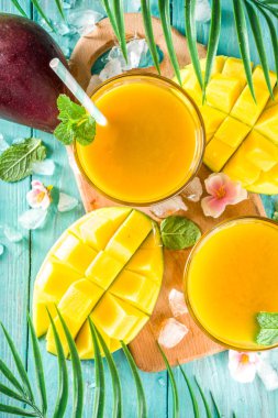 Taze tropikal meyve suyu. Mango smoothie veya mango suyu, taze mango ve açık hava ahşap arka planında tropikal yapraklar. Üst görünümü kopyala.
