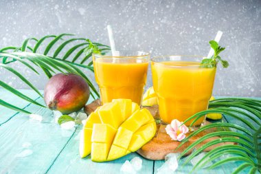 Taze tropikal meyve suyu. Mango smoothie veya mango suyu, taze mango ve açık hava ahşap arka planında tropikal yapraklar. Üst görünümü kopyala.