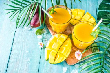 Taze tropikal meyve suyu. Mango smoothie veya mango suyu, taze mango ve açık hava ahşap arka planında tropikal yapraklar. Üst görünümü kopyala.