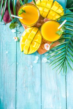 Taze tropikal meyve suyu. Mango smoothie veya mango suyu, taze mango ve açık hava ahşap arka planında tropikal yapraklar. Üst görünümü kopyala.