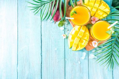 Taze tropikal meyve suyu. Mango smoothie veya mango suyu, taze mango ve açık hava ahşap arka planında tropikal yapraklar. Üst görünümü kopyala.
