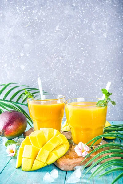 Fresh summer tropical fruit drink. Mango smoothie or mango juice, with fresh mango and tropical leaves on outdoor wooden background. Copy space top view.
