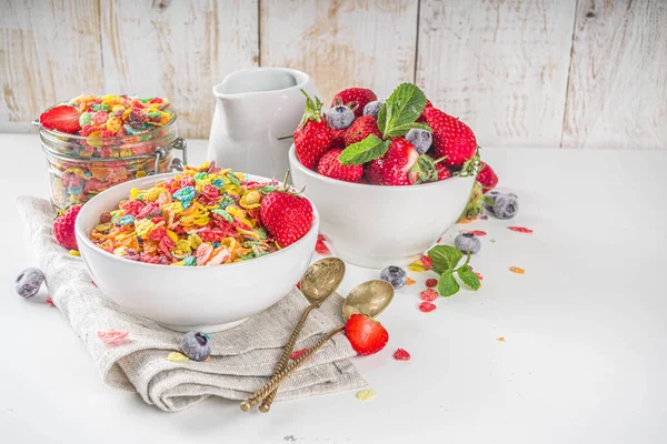 Colorful fruit cereal flakes. Multicolored fruit breakfast corn flakes, with various fruit taste, with milk and fresh berries on white table. Traditional american morning snack