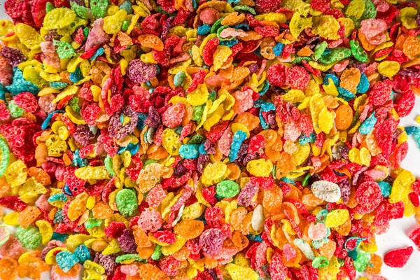 Colorful fruit cereal flakes. Multicolored fruit breakfast corn flakes, with various fruit taste, with milk and fresh berries on white table. Traditional american morning snack